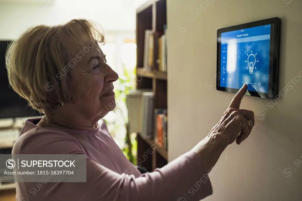 Senior woman touching home automation device on wall