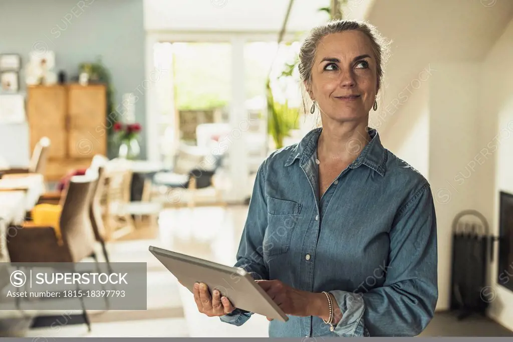 Thoughtful woman with digital tablet standing at home