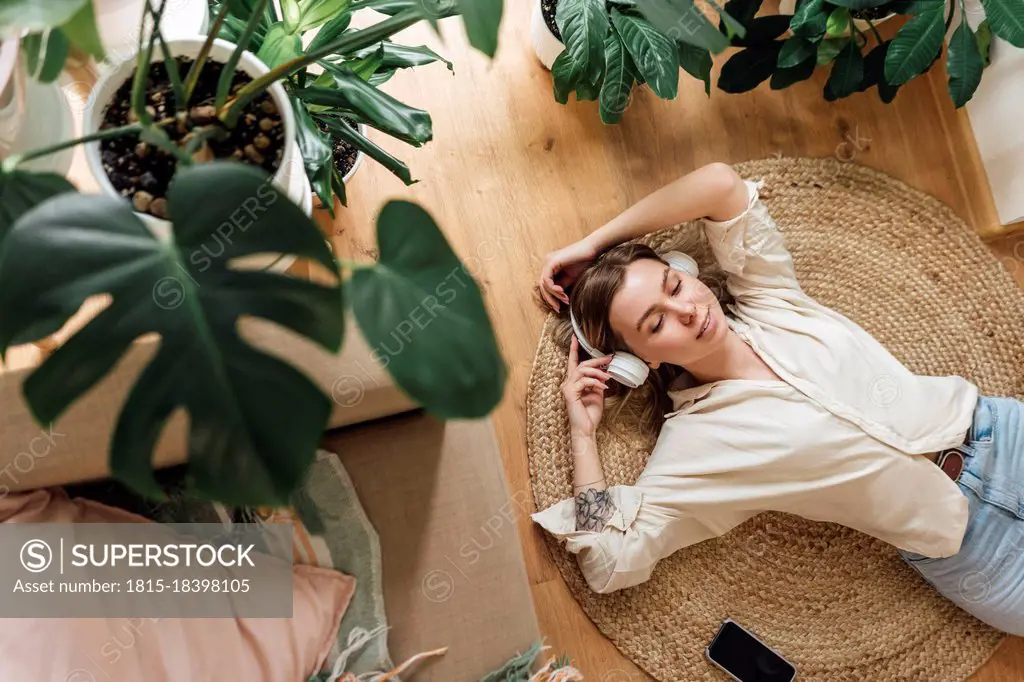 Woman with hands raised listening music while relaxing on rug at home