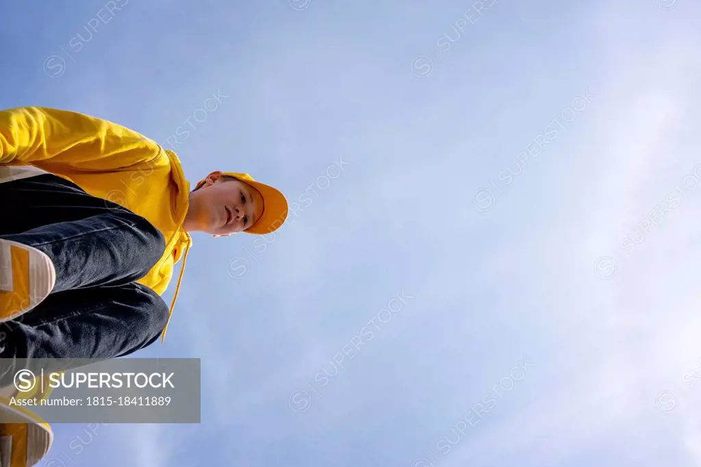 Pre-adolescent boy wearing yellow sweatshirt and cap on sunny day