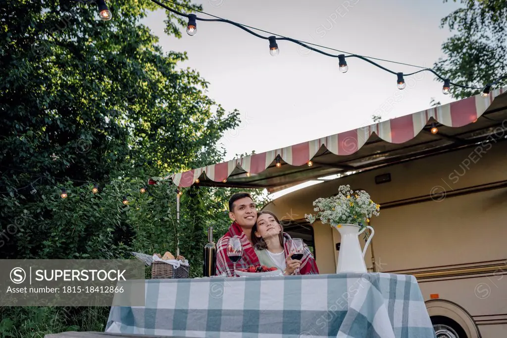 Young couple wrapped in blanket sitting at table by motor home
