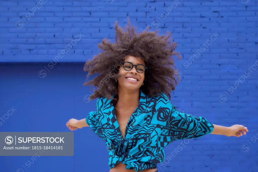 Happy woman dancing with arms outstretched in front of blue wall