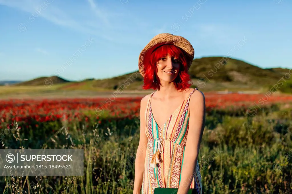 Smiling redheaded woman standing at poppy field