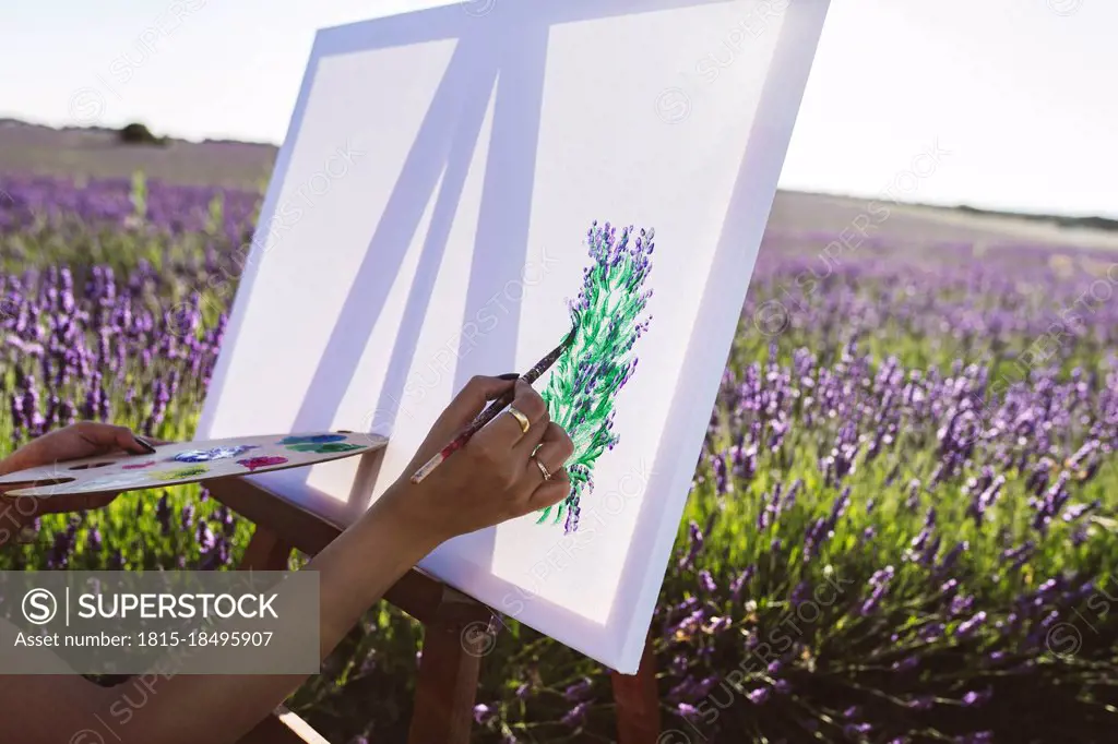 Young woman painting lavender flowers on canvas in field