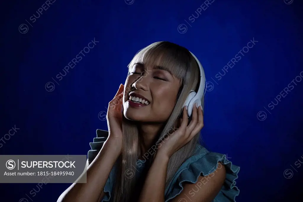 Smiling woman listening music on headphones against blue background