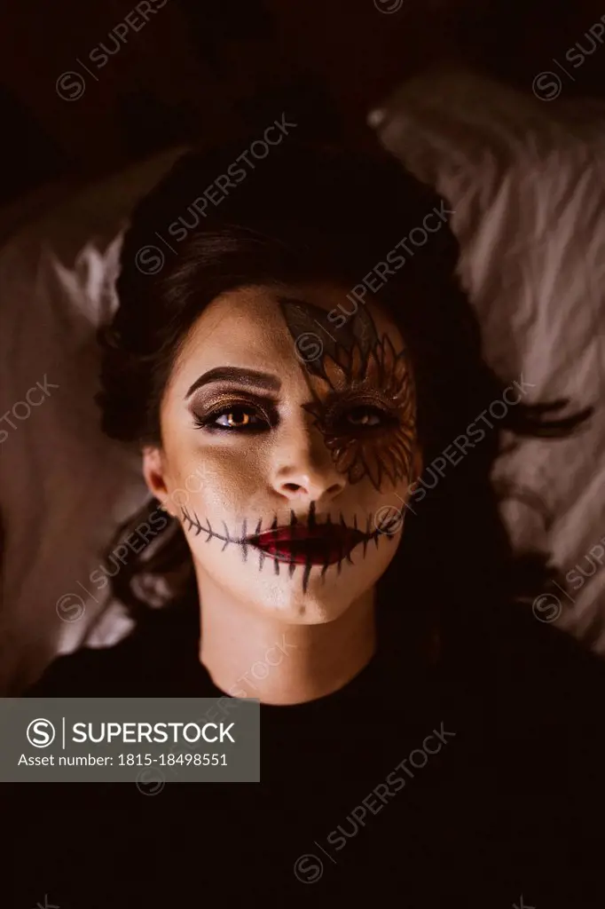 Woman with ceremonial make-up lying on bed during Halloween