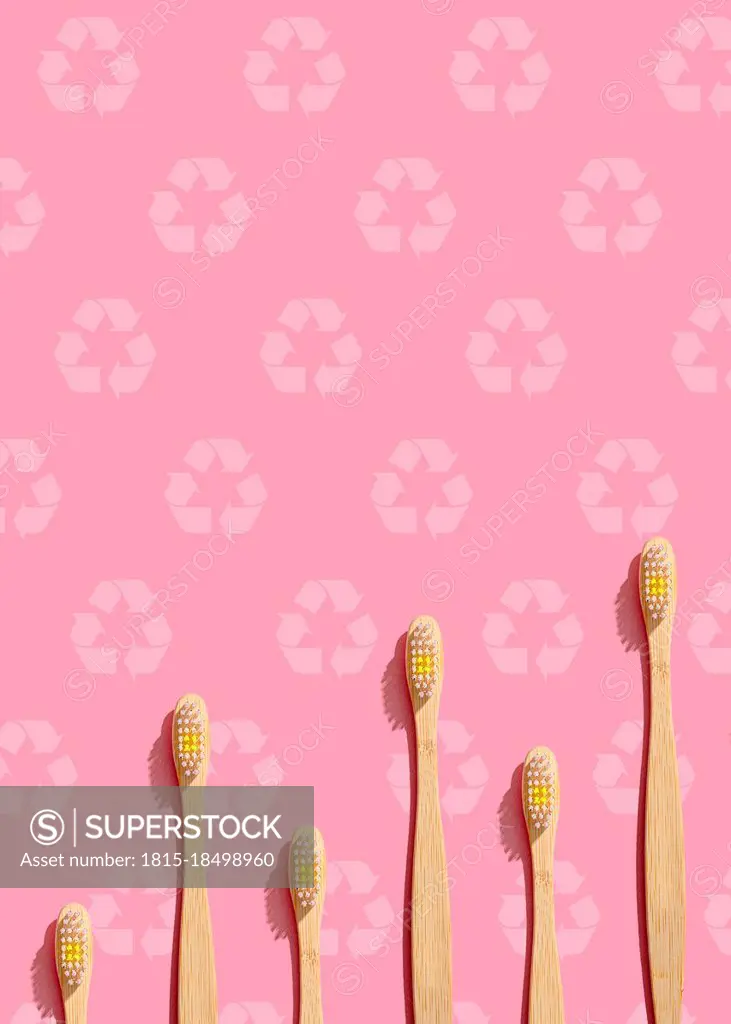 Pattern of wooden toothbrushes flat laid against pink background with recycling symbols