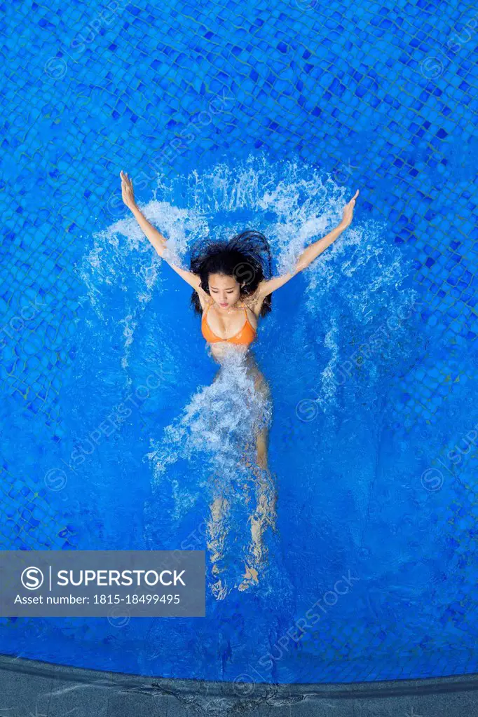 Young woman splashing water while swimming in pool