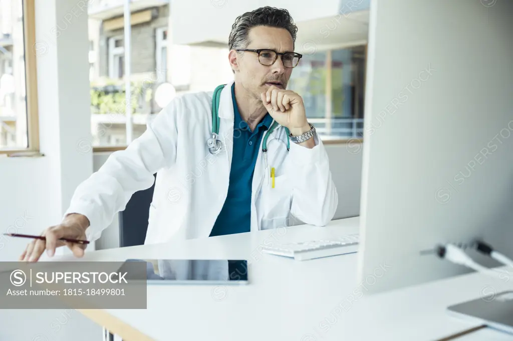 Male doctor with hand on chin using computer at office
