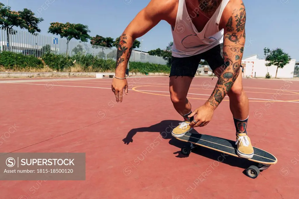 Young man skateboarding at basketball court during sunny day