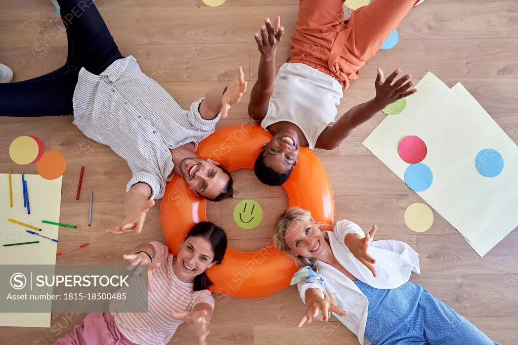 Happy male and female colleagues lying on inflatable ring in office