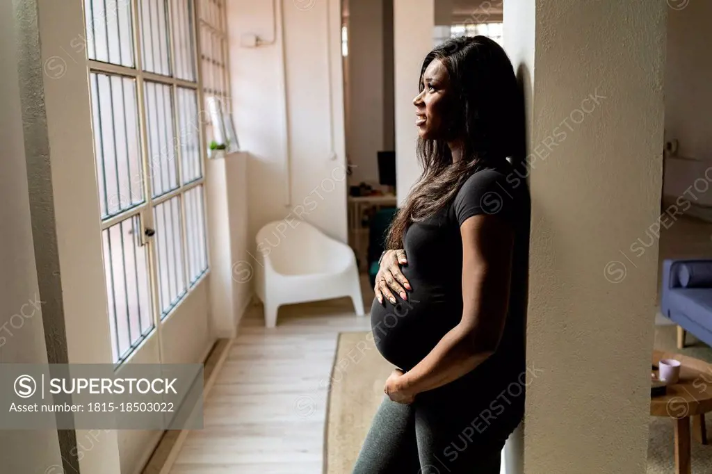 Thoughtful young pregnant woman leaning against column at home