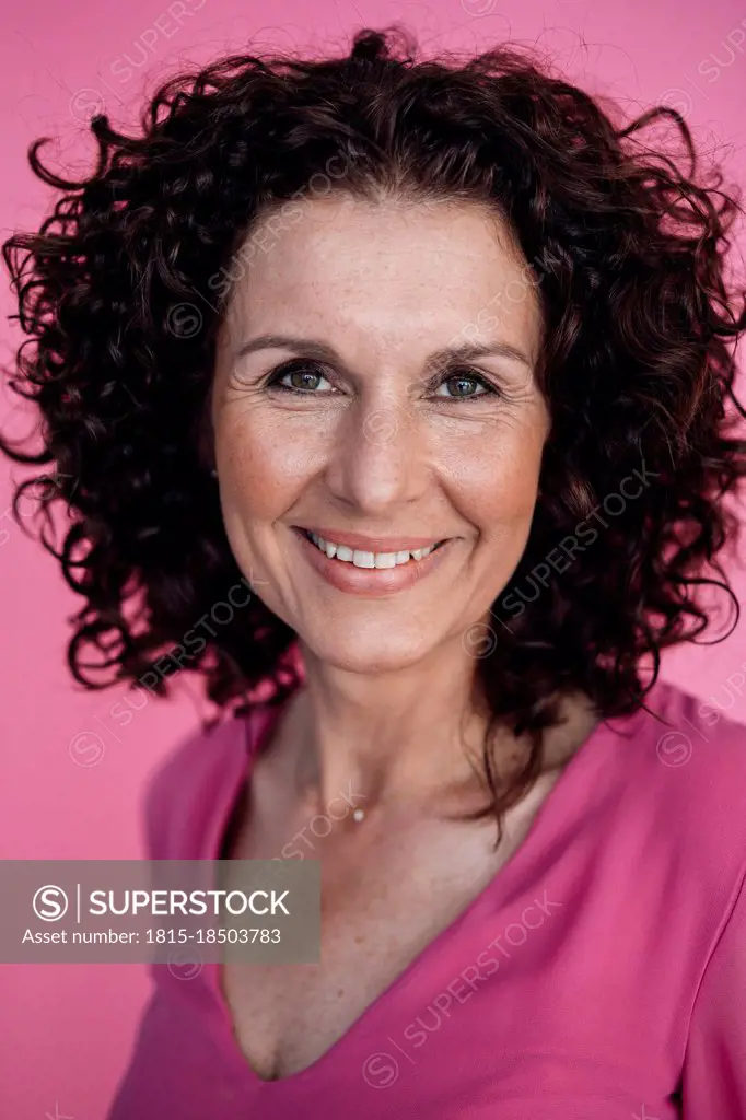 Curly haired businesswoman smiling over pink background