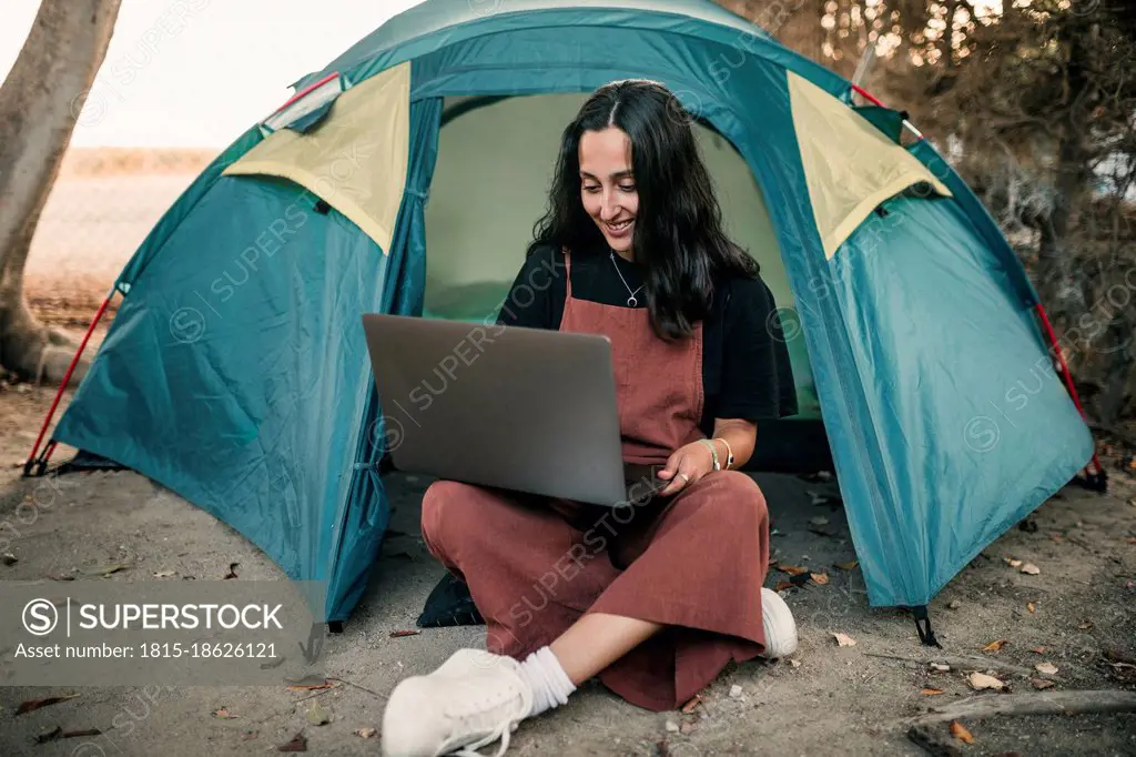 Smiling female freelancer working on laptop while sitting in tent during weekend