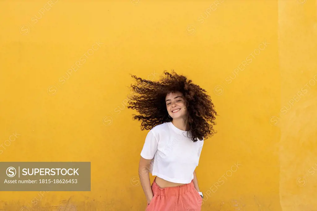 Carefree woman tossing hair in front of yellow wall