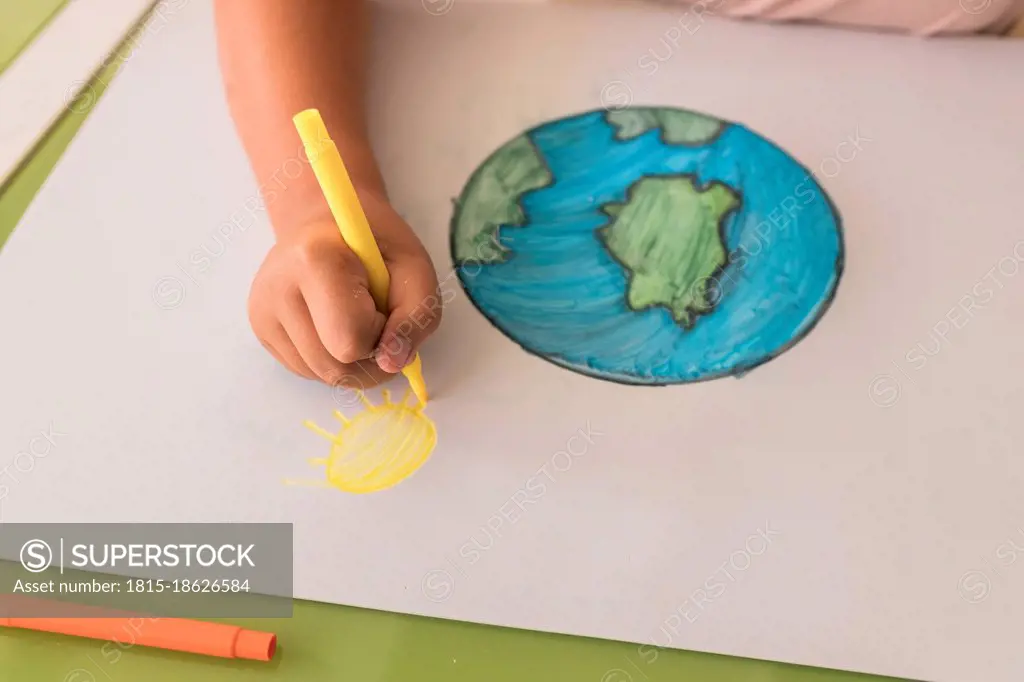 Girl drawing sun on cardboard paper at home