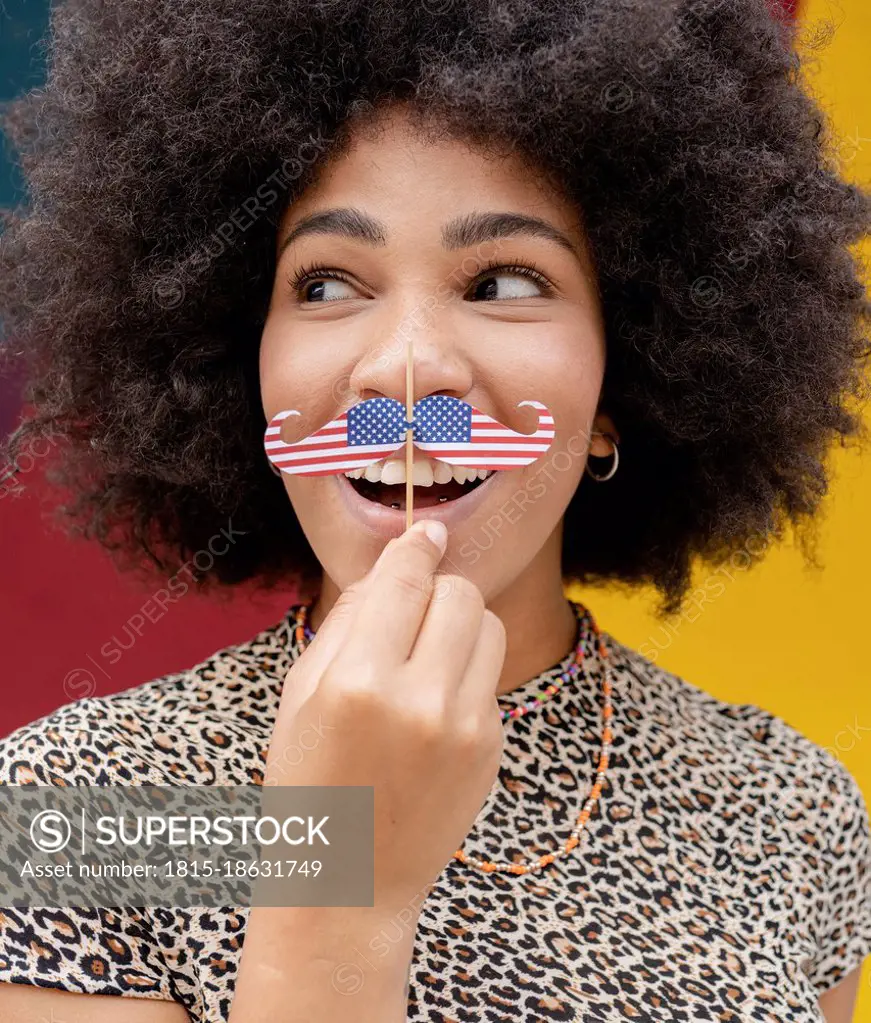 Woman looking sideways while holding mustache prop