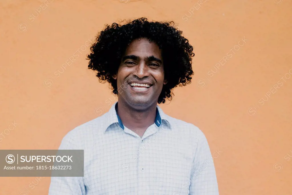 Happy man with curly black hair in front of beige wall