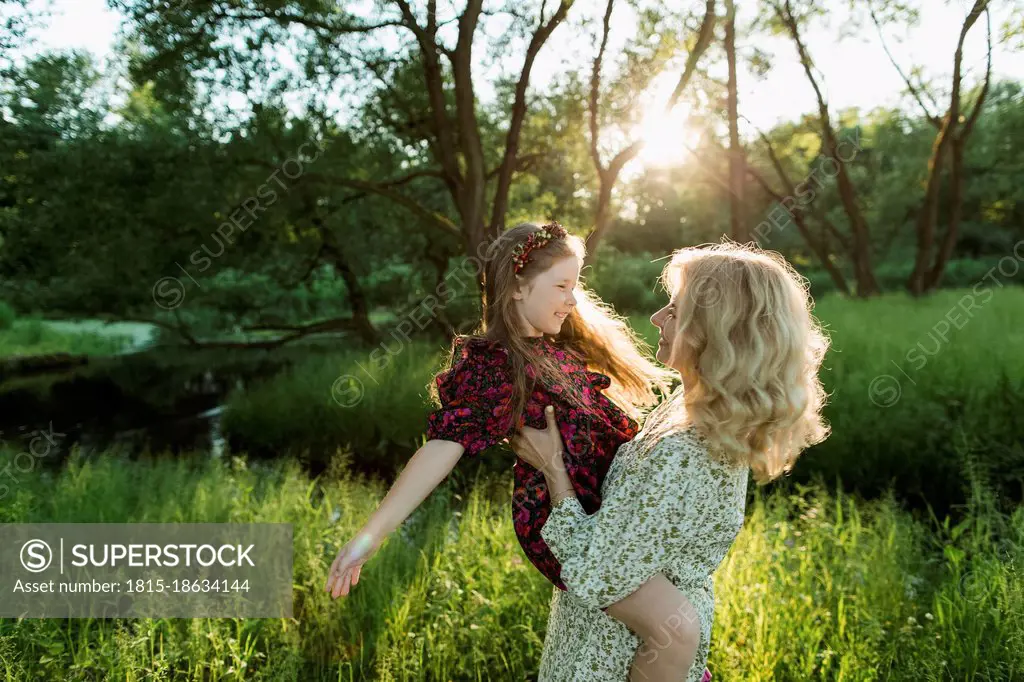 Mother carrying playful daughter during sunset
