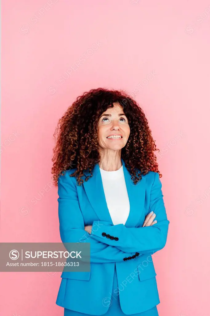 Businesswoman with arms crossed looking up against pink background