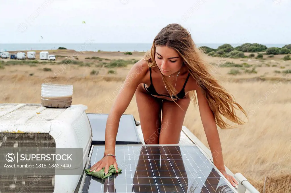 Beautiful woman cleaning solar panel of camper van