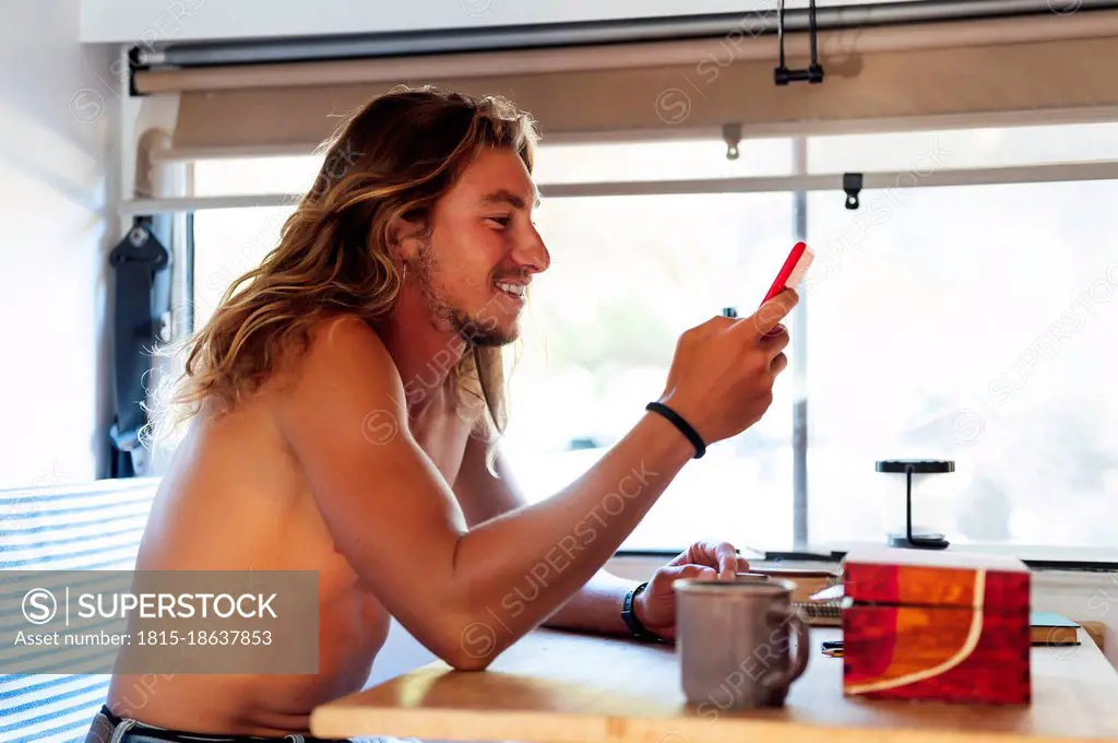 Smiling hipster man using mobile phone while smoking in motor home
