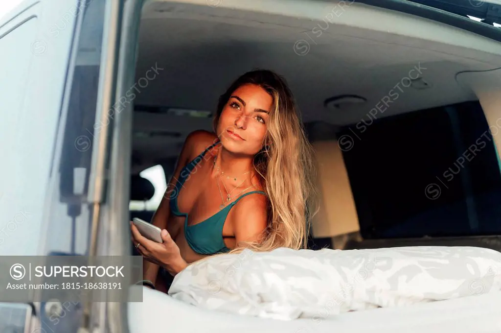 Young woman with mobile phone resting in camper van