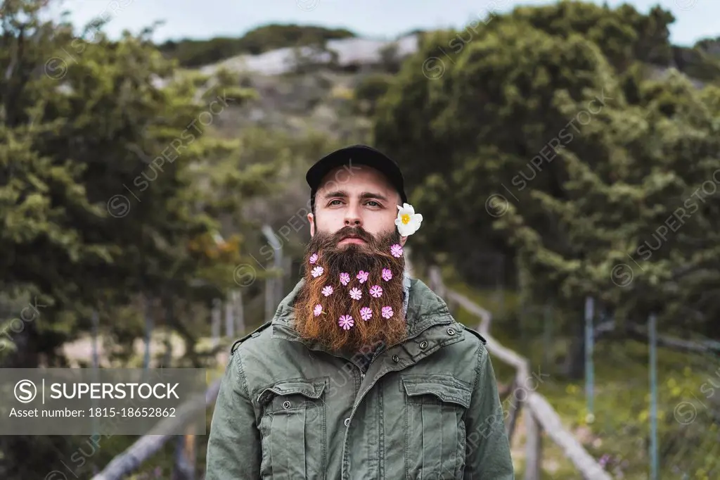 Young man wearing flowers in beard standing on bridge