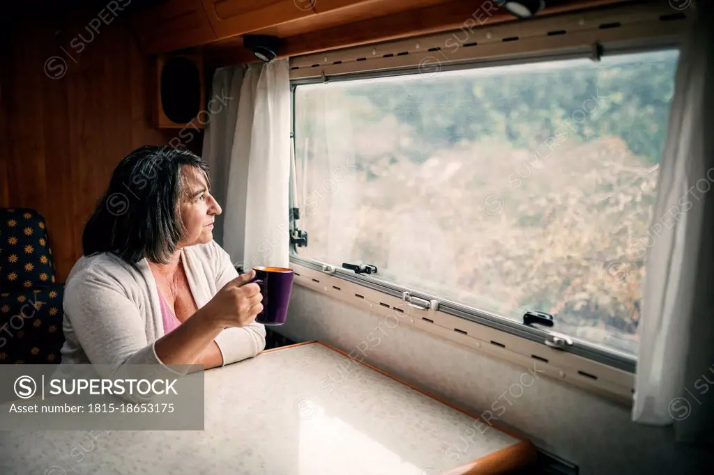 Woman with coffee cup looking through motor home window