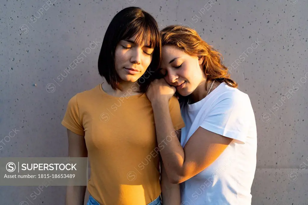 Lesbian couple with eyes closed in front of gray wall
