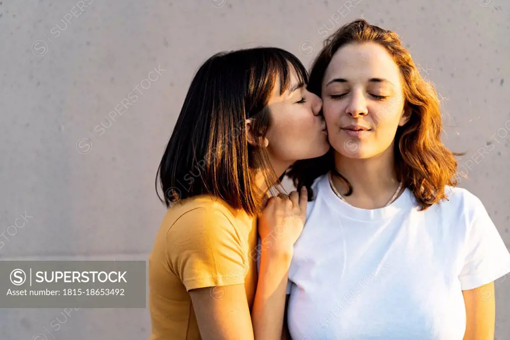 Woman with eyes closed kissing girlfriend in front of wall