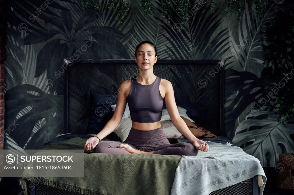 Mid adult woman with eyes closed practicing yoga in bedroom at home