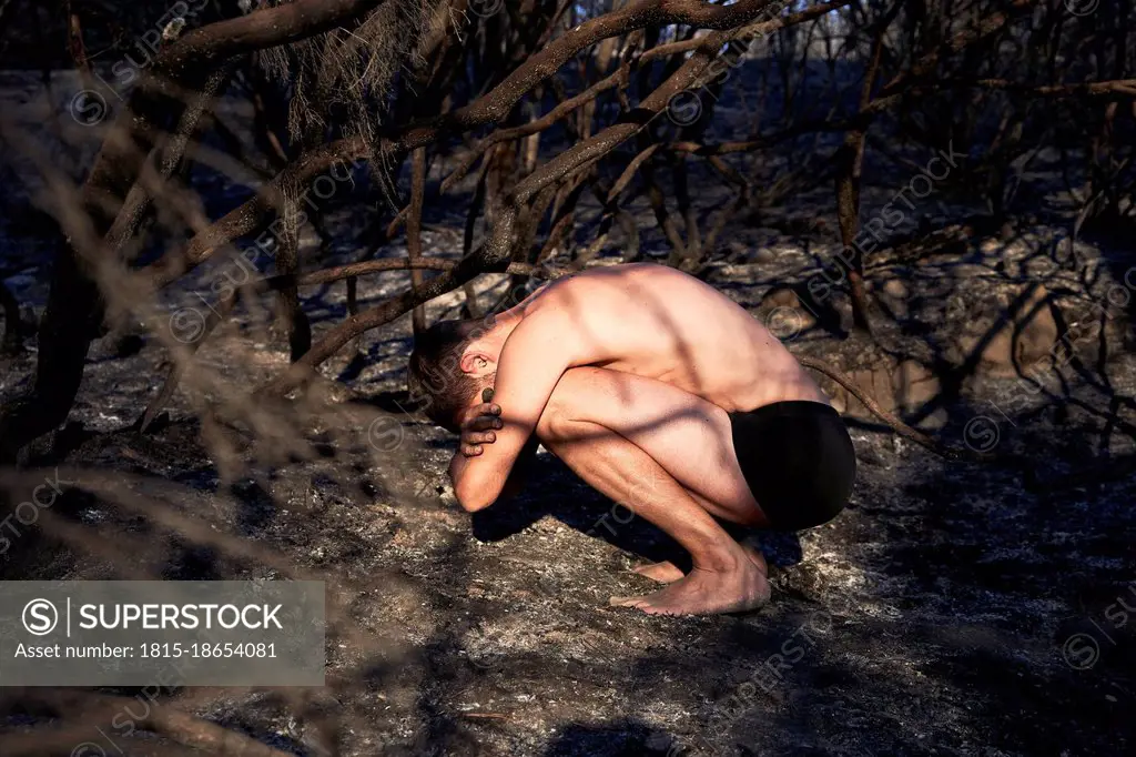 Shirtless man crouching on forest floor