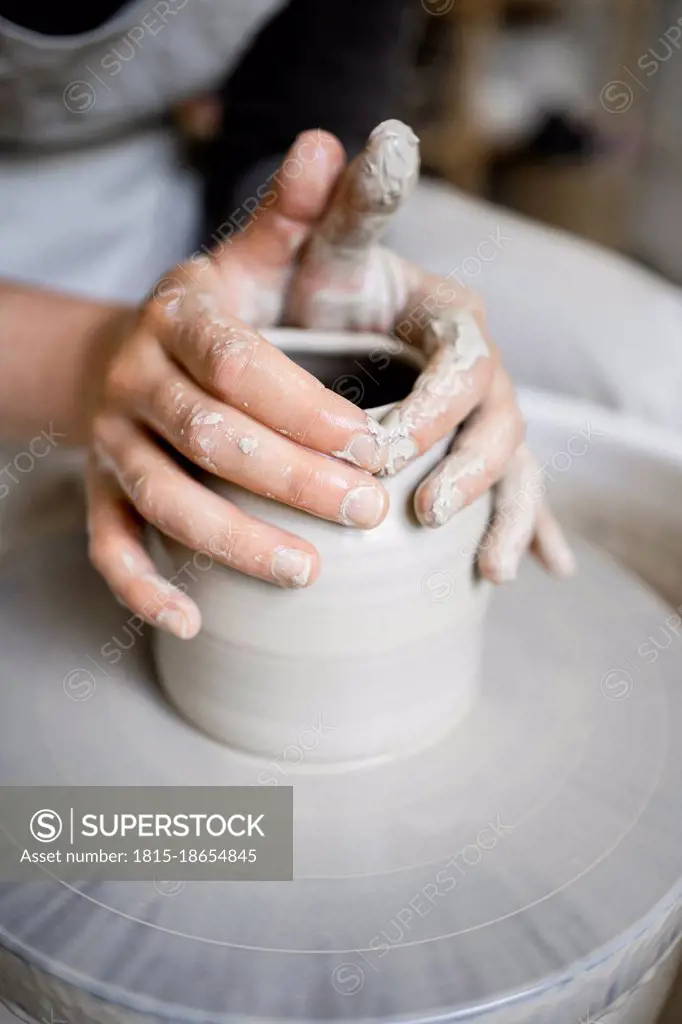 Young female potter making shape on pottery wheel in workshop
