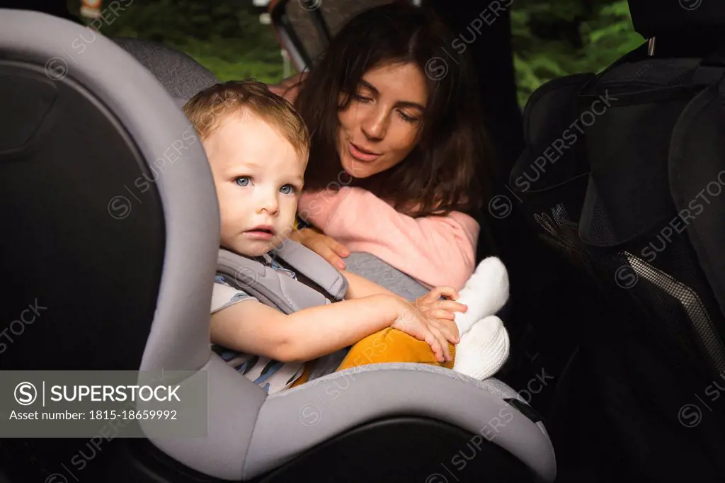 Mother talking to male toddler sitting on baby seat in car