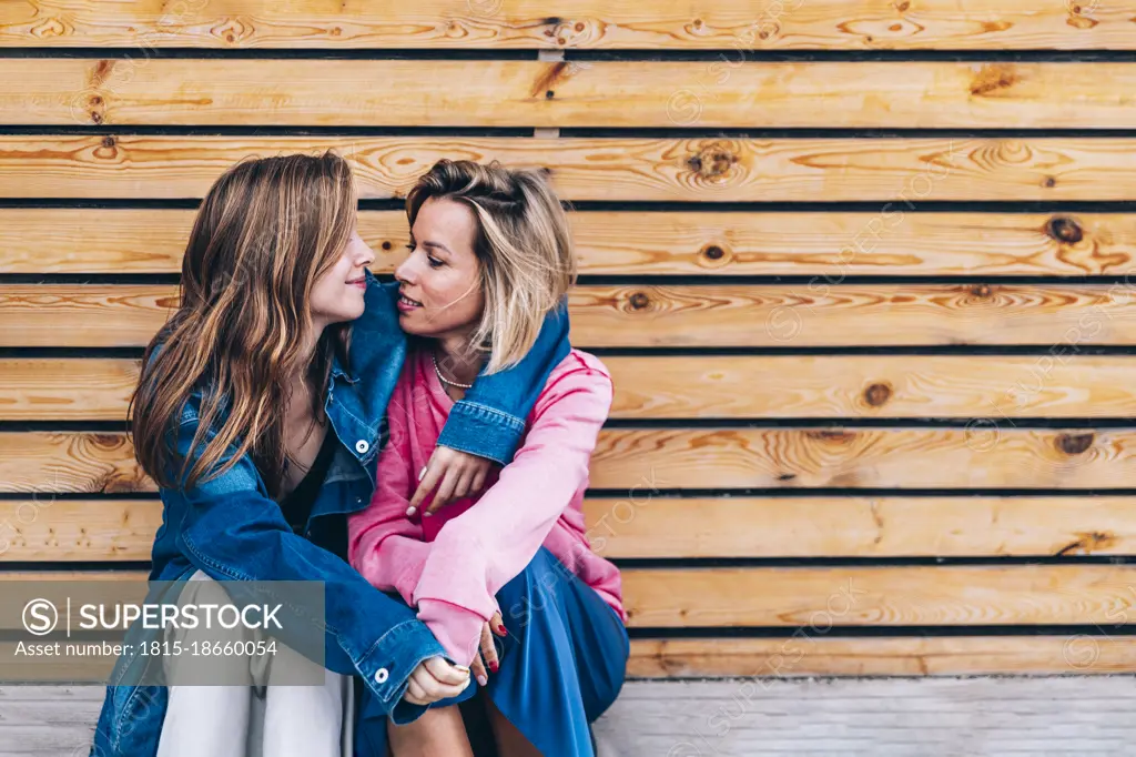 Teenage daughter with mother sitting in front of wooden wall