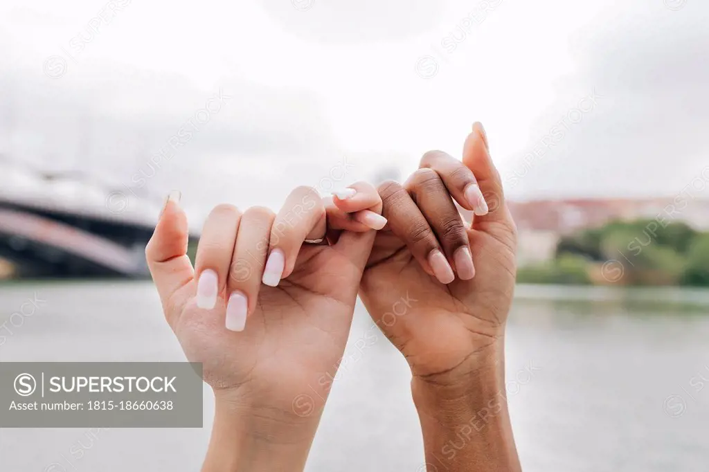 Lesbian couple holding fingers by lake