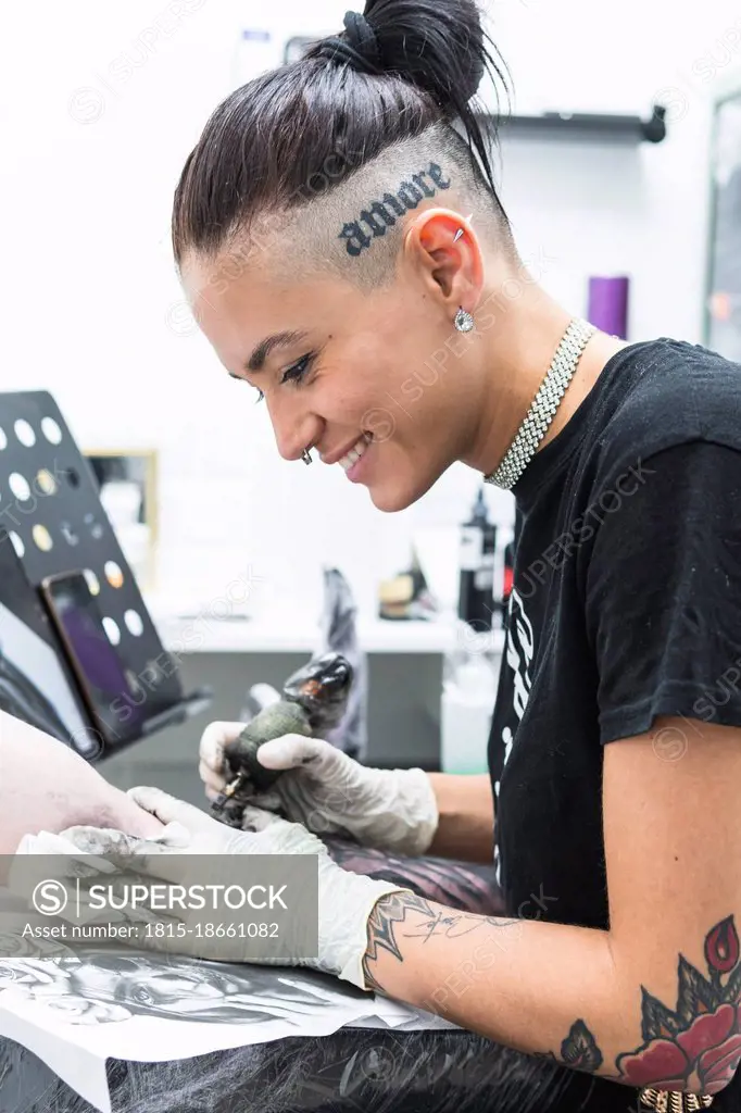 Smiling female artist tattooing on male customer's arm in studio