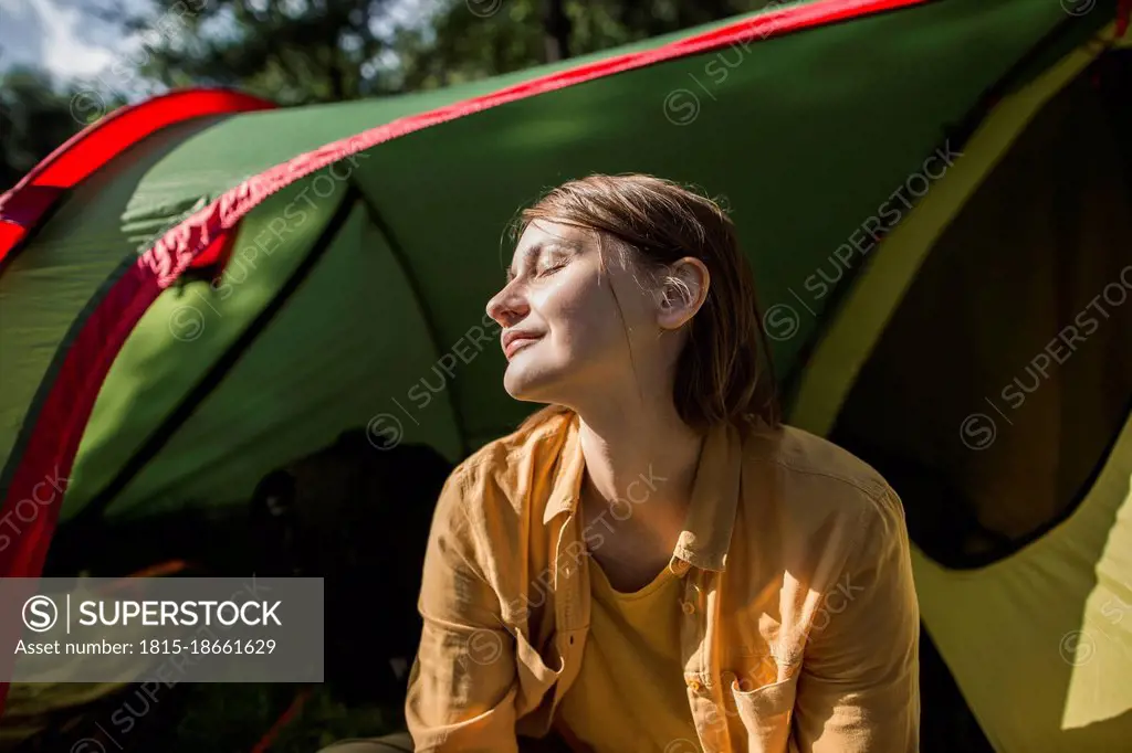 Smiling woman with eyes closed sitting at tent entrance