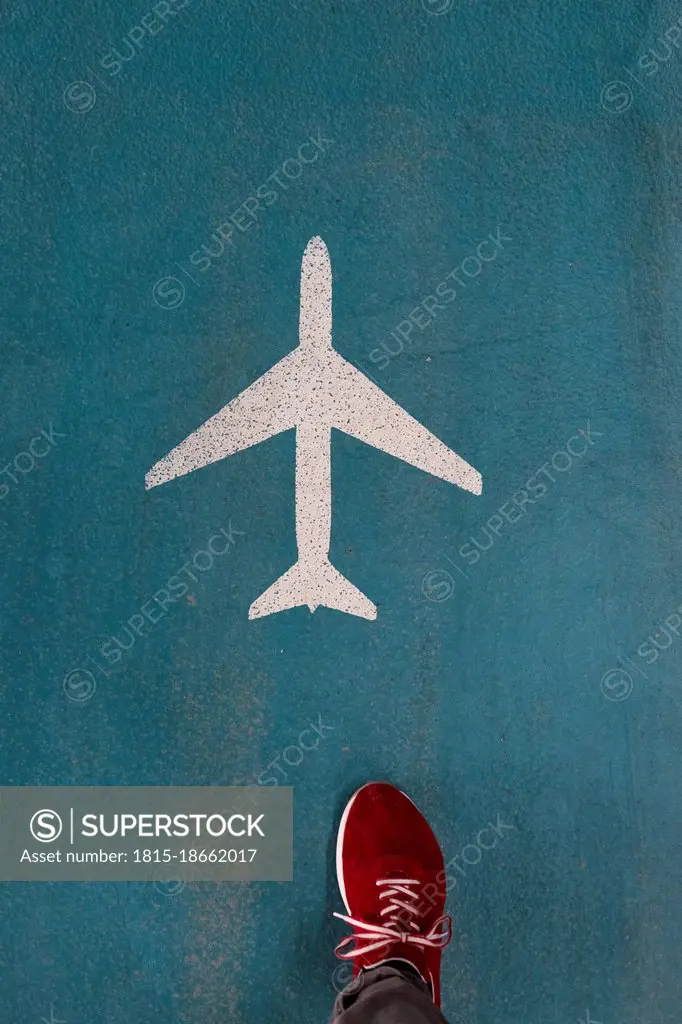 Shoe of person stepping over airplane symbol painted on airport floor