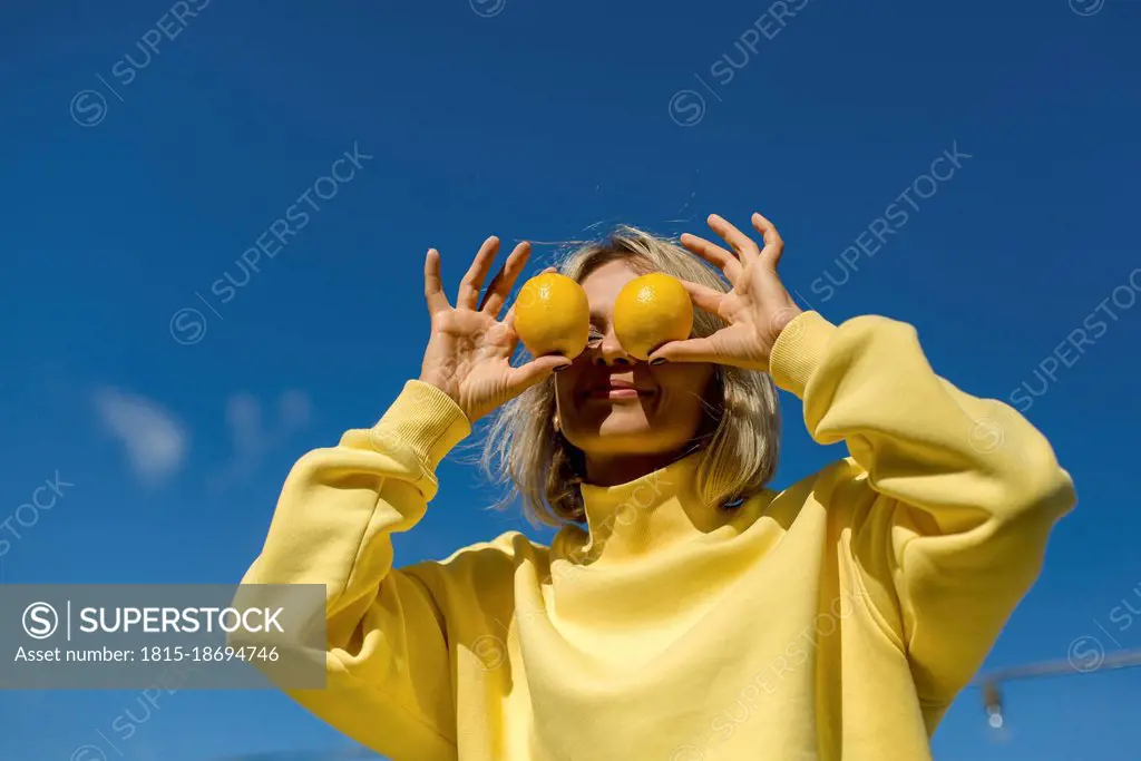 Mid adult woman covering eyes with lemon during sunny day