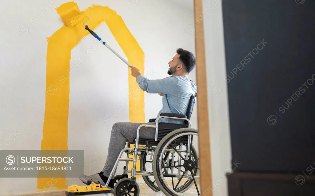 Man with disability painting wall through paint roller at home