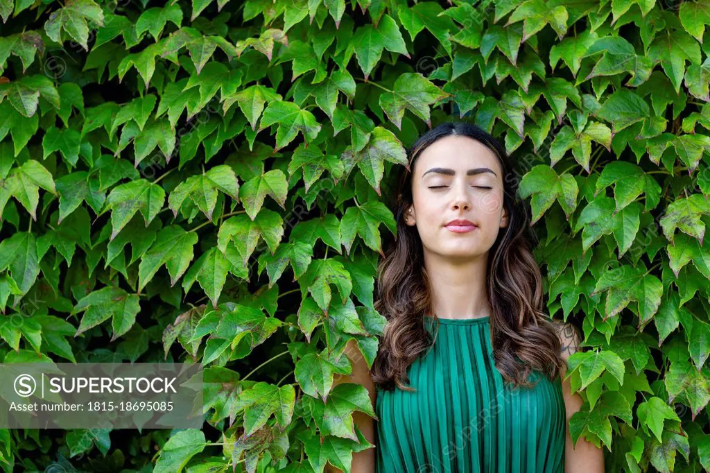 Beautiful young woman with eyes closed leaning on ivy leaves