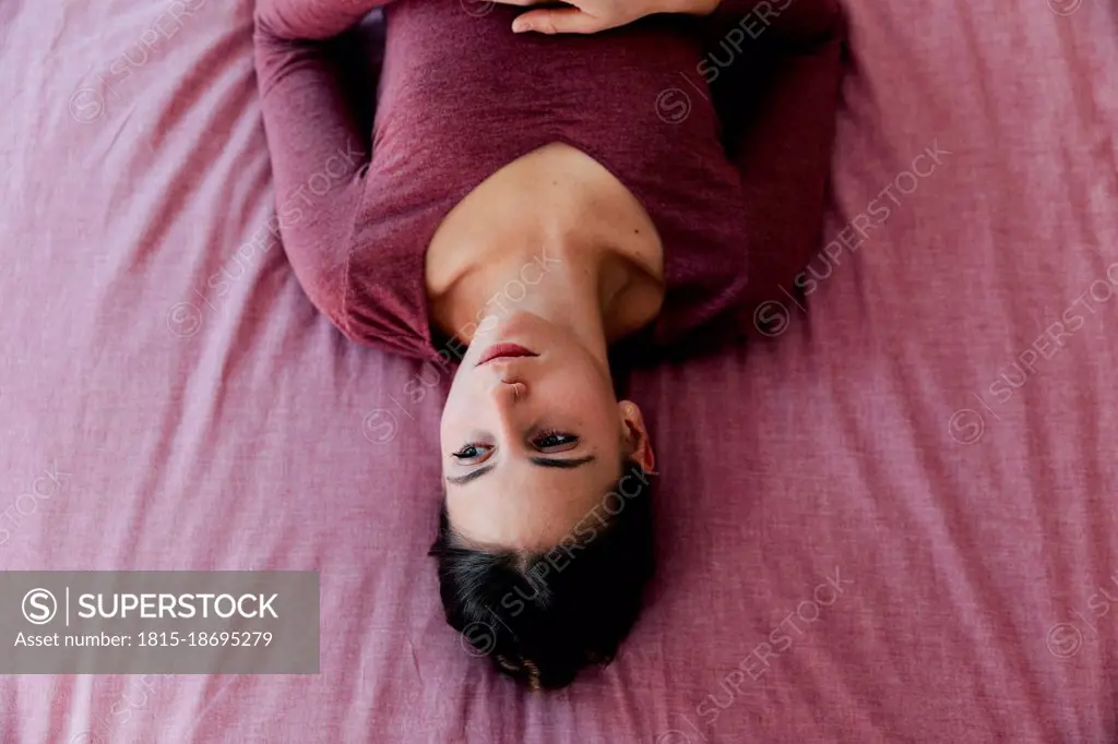 Worried young woman lying on pink bed