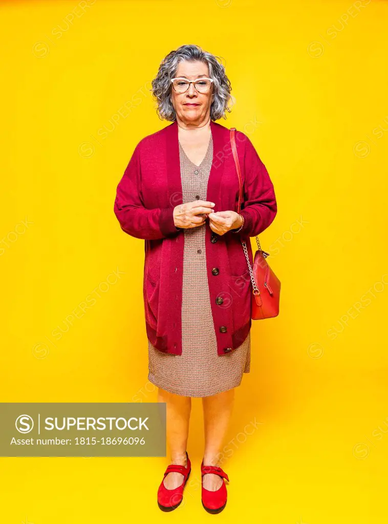 Senior woman with side bag standing in front of yellow background