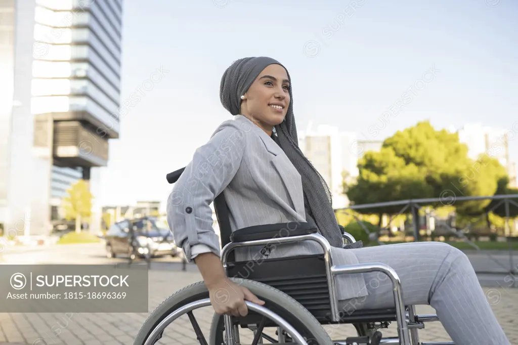 Smiling disabled woman sitting on wheelchair at footpath