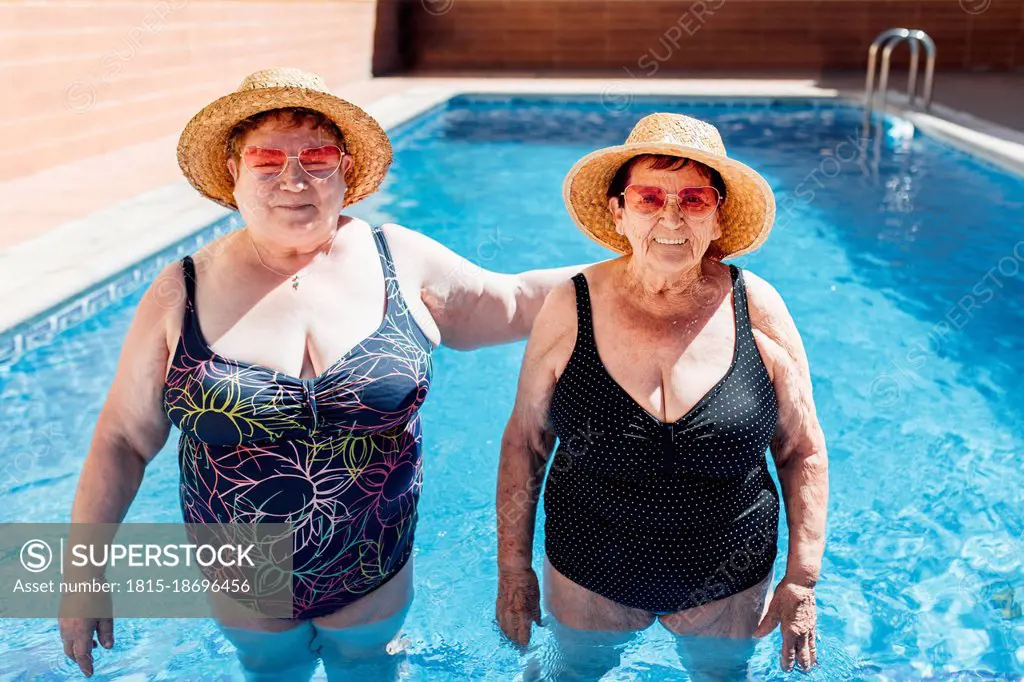 Female friends wearing sun hat standing in swimming pool during vacation