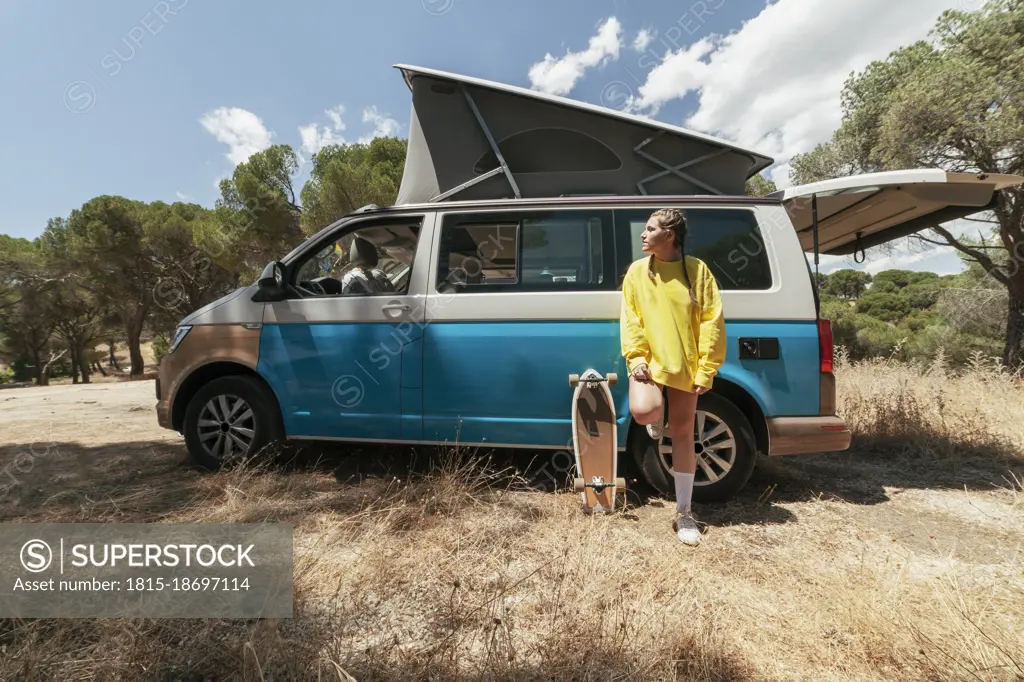 Young woman leaning on camper van on sunny day