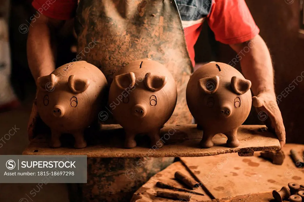 Potter holding plank with clay piggy banks