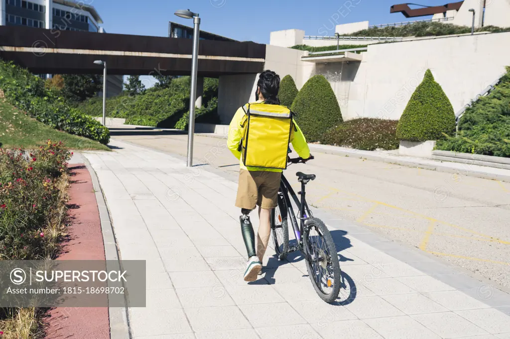Delivery man with prosthetic leg wheeling bicycle on footpath